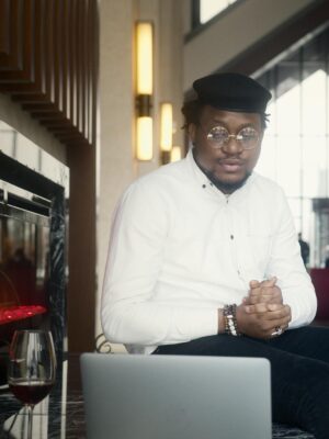 A stylish young man sitting by a laptop in a modern cafe setting, exuding confidence.