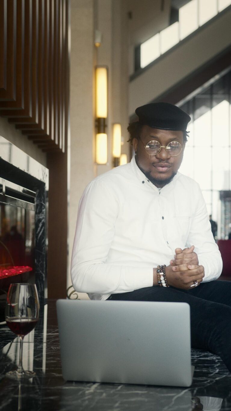A stylish young man sitting by a laptop in a modern cafe setting, exuding confidence.