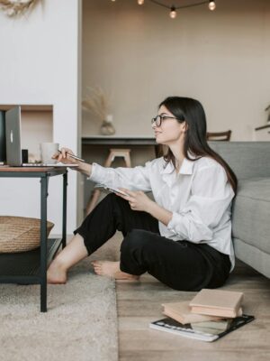 Woman using a laptop while sitting on the floor of a cozy living room, epitomizing work-from-home lifestyle.